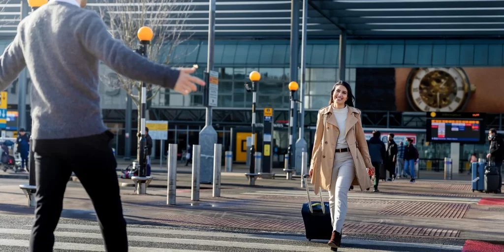 Traveler with luggage warmly greeted by friend outside Heathrow airport terminal in sunshine.webp